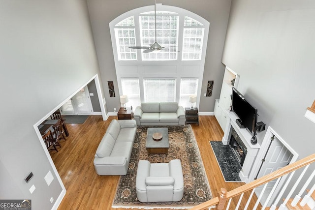 living room with ceiling fan, light wood-type flooring, a fireplace, and a high ceiling