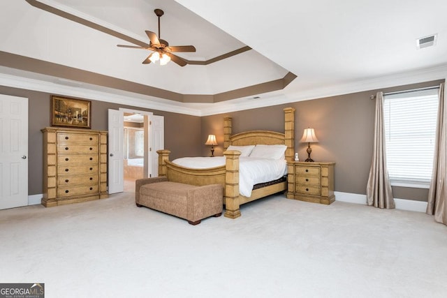 carpeted bedroom with ceiling fan, a raised ceiling, ornamental molding, and ensuite bathroom