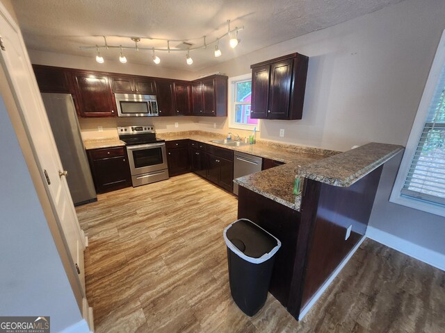 kitchen with a textured ceiling, dark brown cabinetry, stainless steel appliances, a peninsula, and a sink