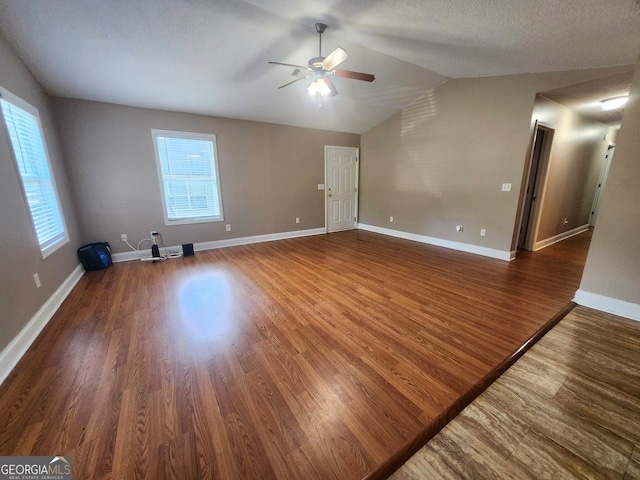 empty room with a textured ceiling, ceiling fan, dark wood-type flooring, and vaulted ceiling