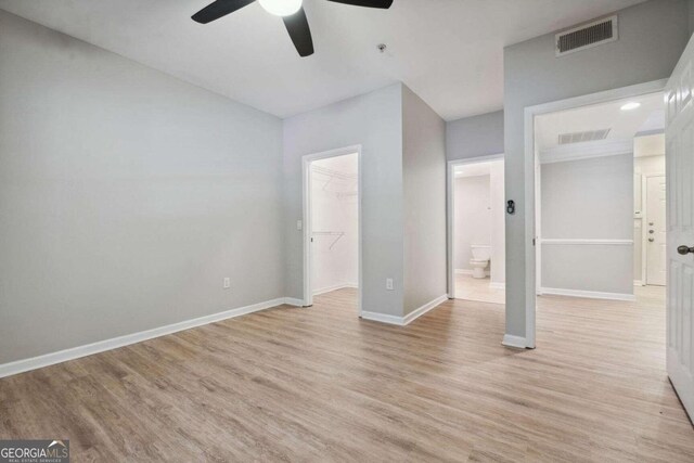 unfurnished bedroom with ensuite bathroom, light hardwood / wood-style flooring, ceiling fan, a spacious closet, and a closet