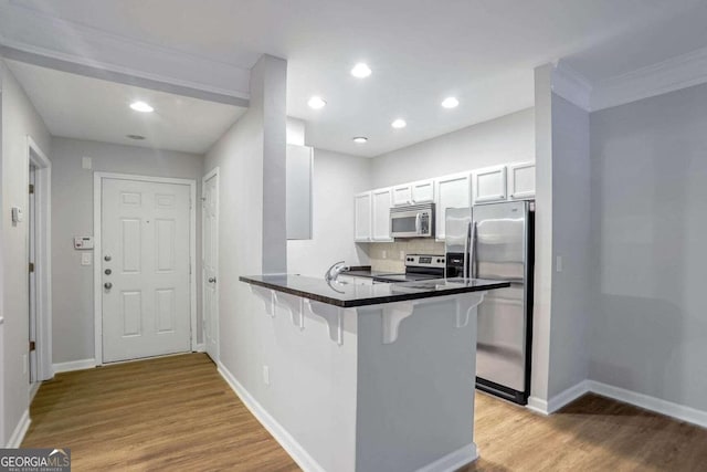 kitchen featuring white cabinetry, a kitchen breakfast bar, kitchen peninsula, decorative backsplash, and appliances with stainless steel finishes