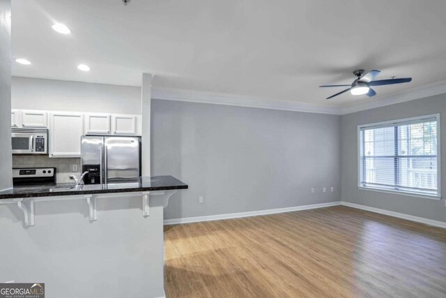 kitchen with decorative backsplash, a kitchen breakfast bar, stainless steel appliances, ceiling fan, and white cabinets