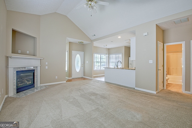 unfurnished living room with ceiling fan, lofted ceiling, sink, a high end fireplace, and light carpet