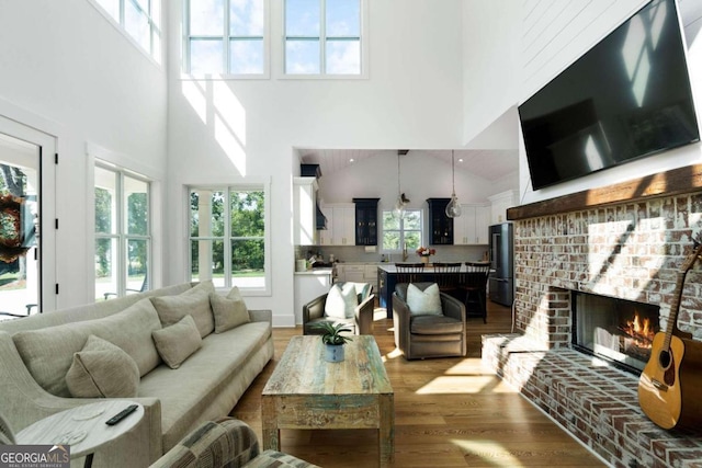 living room with a brick fireplace, a wealth of natural light, high vaulted ceiling, and hardwood / wood-style floors