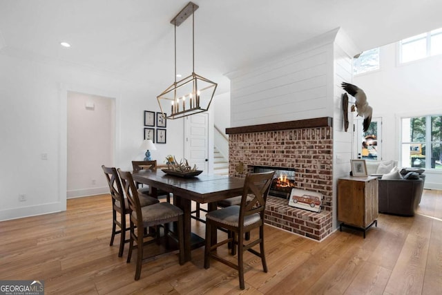 dining space featuring a brick fireplace, an inviting chandelier, light hardwood / wood-style flooring, and a towering ceiling