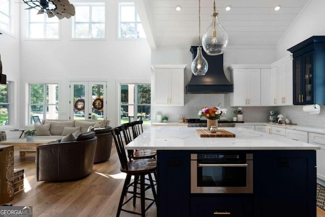 kitchen with white cabinets, light hardwood / wood-style flooring, stainless steel oven, custom range hood, and a center island