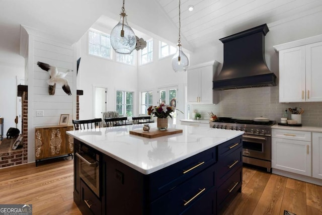 kitchen featuring custom range hood, white cabinets, a kitchen island, stainless steel appliances, and light hardwood / wood-style flooring