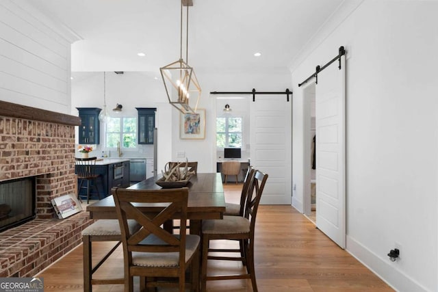 dining room featuring a brick fireplace, wood-type flooring, plenty of natural light, and a barn door