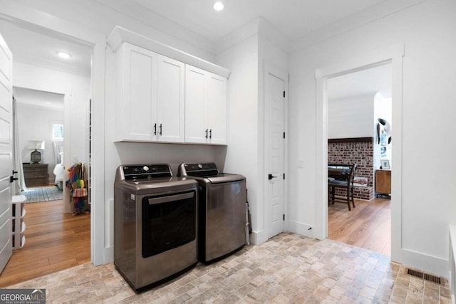 clothes washing area featuring washer and clothes dryer, ornamental molding, cabinets, and light hardwood / wood-style floors