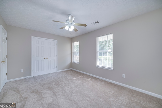 unfurnished bedroom with ceiling fan, a textured ceiling, a closet, and light colored carpet