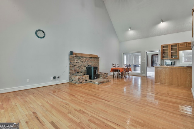 unfurnished living room with high vaulted ceiling, a brick fireplace, light hardwood / wood-style flooring, and plenty of natural light