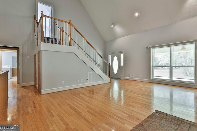 unfurnished living room featuring light hardwood / wood-style floors, washer / clothes dryer, and high vaulted ceiling