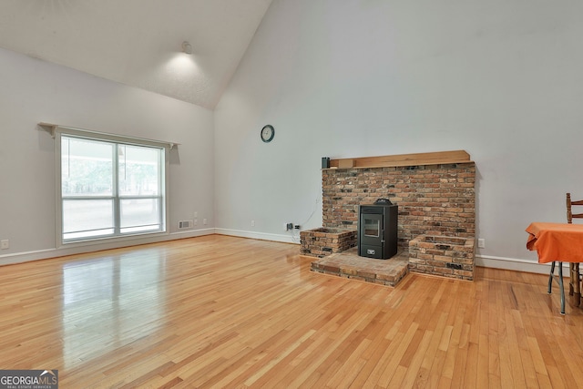 unfurnished living room with light hardwood / wood-style floors, a wood stove, and high vaulted ceiling