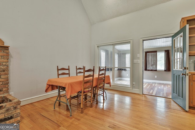 dining room with a textured ceiling, light hardwood / wood-style flooring, and vaulted ceiling