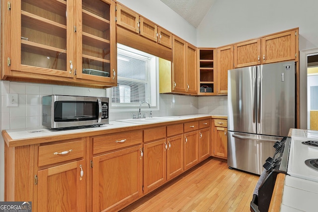 kitchen featuring appliances with stainless steel finishes, a textured ceiling, light wood-type flooring, lofted ceiling, and sink