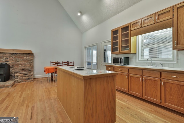 kitchen featuring sink, a kitchen island, a textured ceiling, high vaulted ceiling, and light wood-type flooring