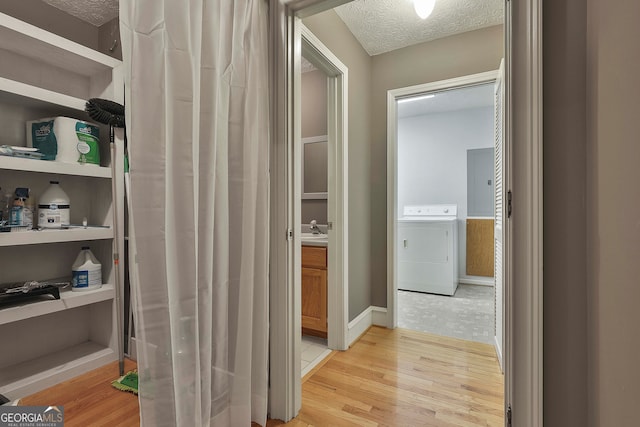 corridor with a textured ceiling, sink, light hardwood / wood-style floors, and washer / dryer