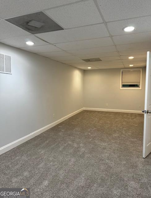 basement with a drop ceiling and dark colored carpet