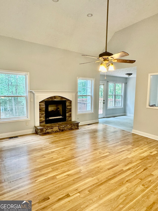 unfurnished living room with light wood-type flooring, vaulted ceiling, ceiling fan, and a stone fireplace