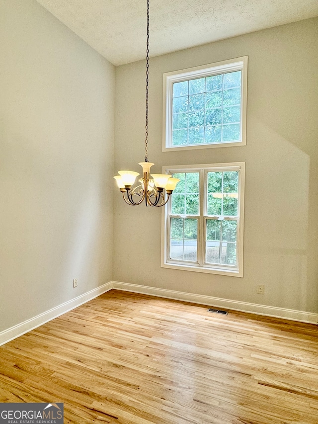 spare room with light hardwood / wood-style flooring, a chandelier, and a textured ceiling