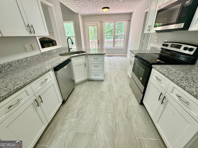 kitchen with appliances with stainless steel finishes, light stone counters, white cabinets, kitchen peninsula, and sink