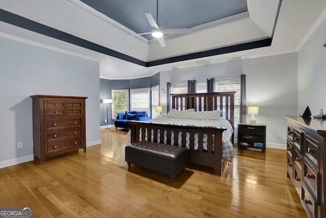 bedroom featuring a raised ceiling, ornamental molding, light wood-type flooring, and ceiling fan