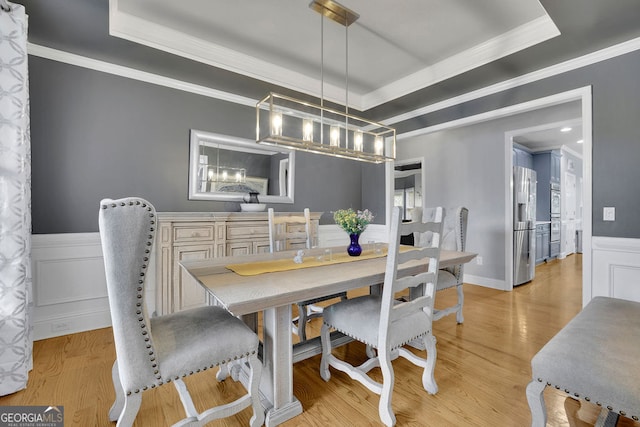 dining space with crown molding, a tray ceiling, and light wood-type flooring