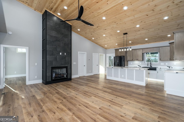 unfurnished living room featuring ceiling fan, wooden ceiling, a high ceiling, hardwood / wood-style floors, and a tiled fireplace