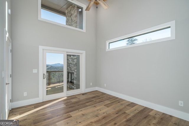 unfurnished room featuring a wealth of natural light, hardwood / wood-style floors, a towering ceiling, and ceiling fan