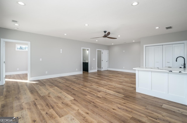 unfurnished living room featuring light wood-type flooring, ceiling fan, and sink