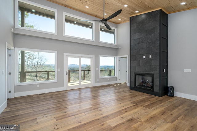 unfurnished living room with ceiling fan, a towering ceiling, wood-type flooring, wood ceiling, and a tiled fireplace