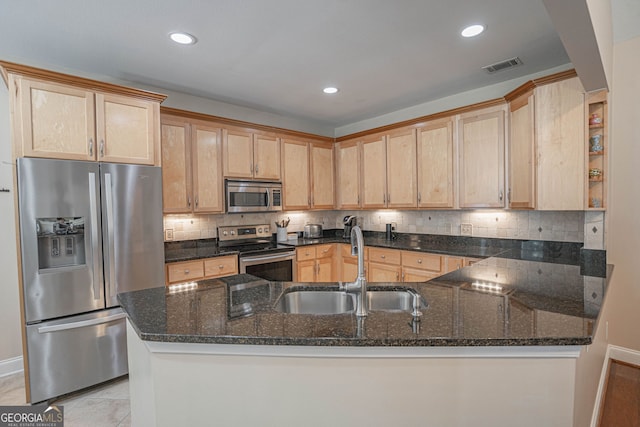 kitchen with appliances with stainless steel finishes, dark stone counters, kitchen peninsula, and sink