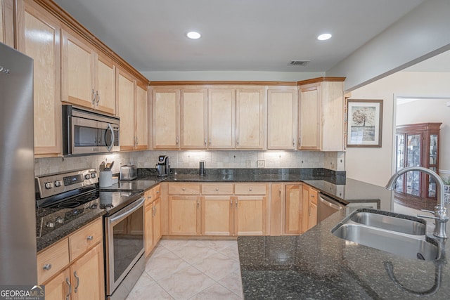 kitchen with appliances with stainless steel finishes, dark stone countertops, tasteful backsplash, light brown cabinetry, and sink