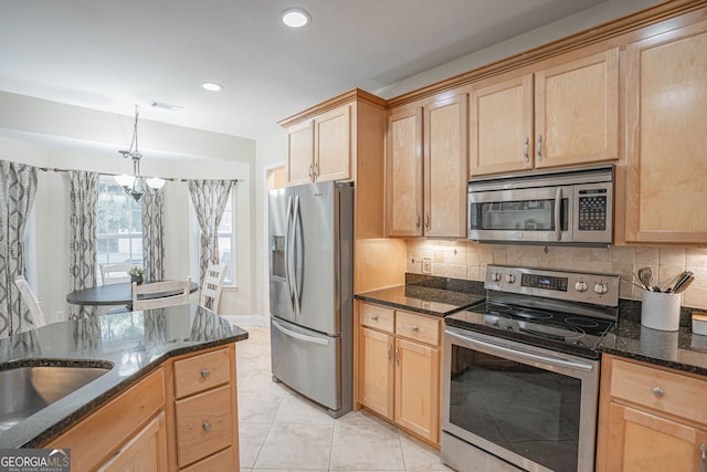 kitchen with a notable chandelier, stainless steel appliances, dark stone counters, and decorative backsplash