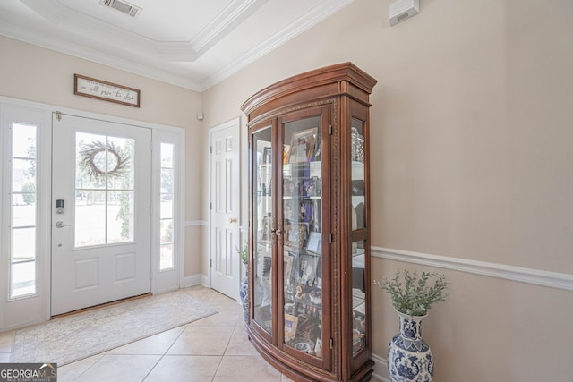 entryway with a healthy amount of sunlight, ornamental molding, light tile patterned floors, and a raised ceiling