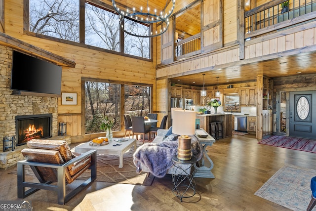 living room with a chandelier, wood walls, a fireplace, a towering ceiling, and dark hardwood / wood-style flooring