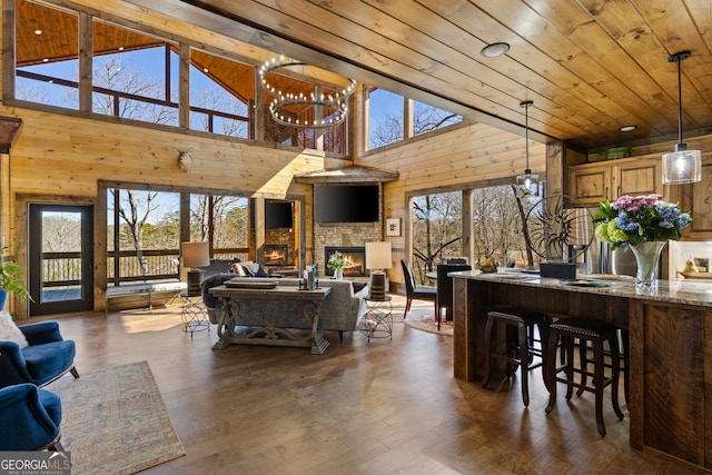 living room featuring a stone fireplace, high vaulted ceiling, wooden ceiling, a notable chandelier, and dark hardwood / wood-style flooring