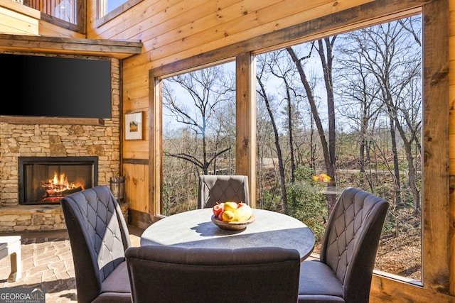 dining space with wooden walls, an outdoor stone fireplace, and plenty of natural light