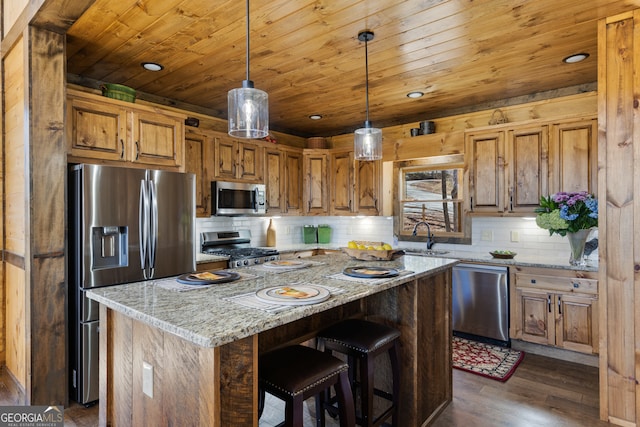 kitchen with appliances with stainless steel finishes, hanging light fixtures, dark wood-type flooring, light stone counters, and a kitchen island