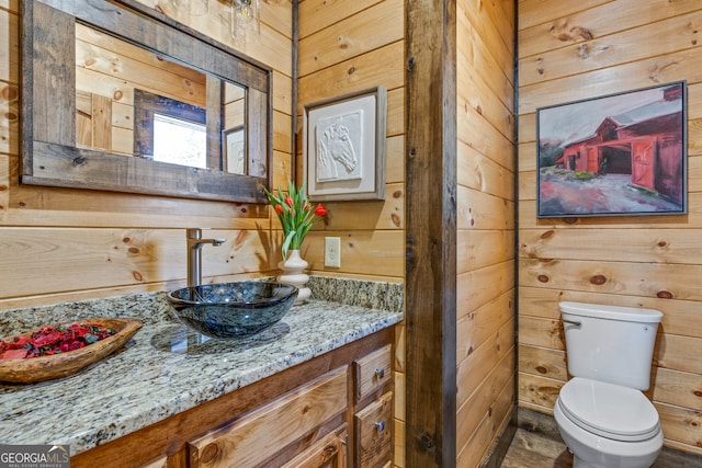 bathroom featuring vanity, wood walls, and toilet