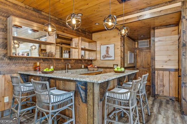 kitchen featuring light stone counters, kitchen peninsula, wood walls, decorative light fixtures, and dark hardwood / wood-style floors