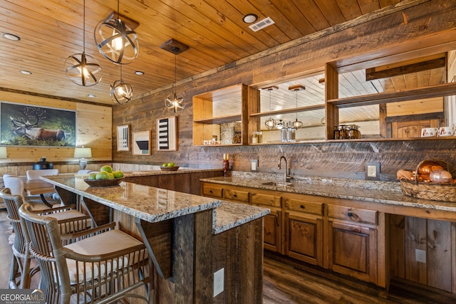 kitchen featuring light stone counters, pendant lighting, sink, wooden walls, and dark hardwood / wood-style flooring