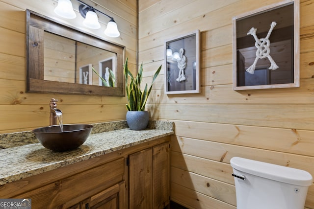 bathroom with vanity, wooden walls, and toilet