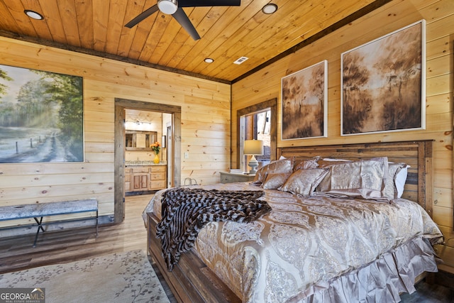 bedroom featuring wood-type flooring, connected bathroom, wood walls, and ceiling fan