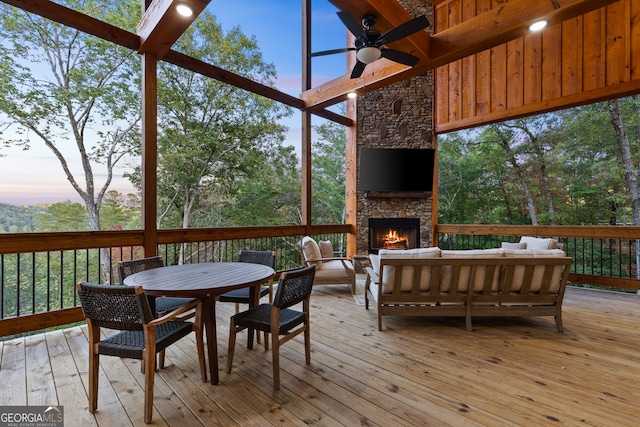 sunroom featuring beam ceiling, an outdoor stone fireplace, and ceiling fan