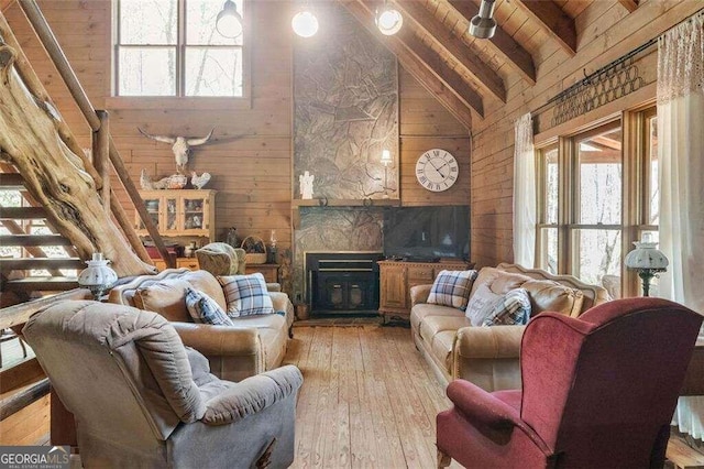 living room featuring wood ceiling, light wood-type flooring, beam ceiling, a fireplace, and wooden walls