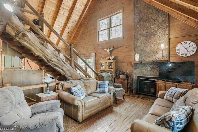 living room with wood ceiling, wood-type flooring, a stone fireplace, wooden walls, and high vaulted ceiling