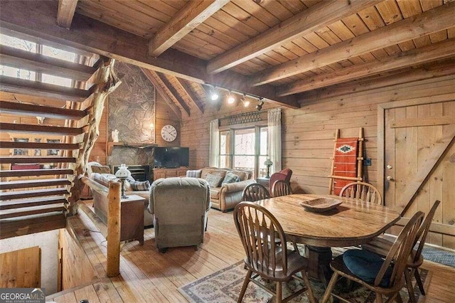 dining area featuring vaulted ceiling with beams, a stone fireplace, wood ceiling, and light hardwood / wood-style floors