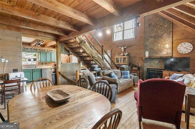 dining space with wood ceiling, lofted ceiling with beams, wood walls, a fireplace, and light hardwood / wood-style flooring